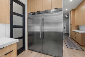 Kitchen featuring light stone counters, light brown cabinetry, light wood-style flooring, stainless steel built in refrigerator, and recessed lighting