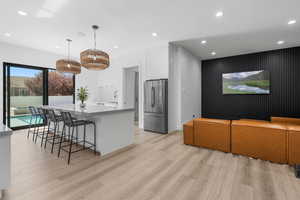 Outdoor living area with Kitchen featuring recessed lighting, freestanding refrigerator, light wood-style floors, a center island with sink, and white cabinetry