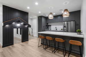 Lower level Kitchenette with light wood finished floors, stainless steel fridge, light countertops, decorative light fixtures, and a breakfast bar area