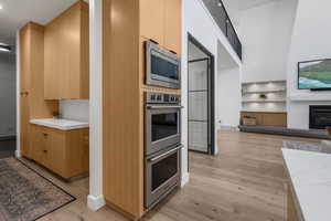Kitchen featuring stainless steel appliances, a glass covered fireplace, visible vents, light wood-style floors, and modern cabinets