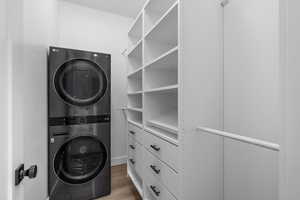 Clothes washing area with light wood-style floors, stacked washer / dryer, and laundry area
