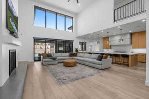 Living area featuring a high ceiling, light wood-style floors, a fireplace with raised hearth, and baseboards