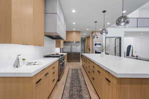Kitchen with a large island, custom exhaust hood, light wood-style floors, built in appliances, and modern cabinets