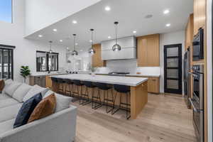 Kitchen featuring light wood finished floors, stainless steel appliances, open floor plan, a kitchen bar, and premium range hood