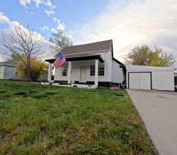 Bungalow-style home with a front lawn, covered porch, an outbuilding, and concrete driveway
