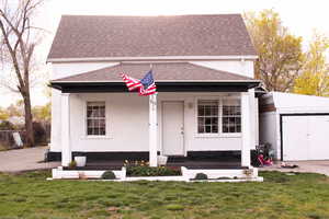 Bungalow featuring an outdoor structure, a shingled roof, a front lawn, and stucco siding