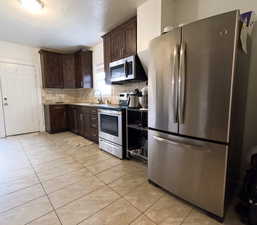 Kitchen featuring backsplash, light tile patterned floors, a sink, dark brown cabinetry, and appliances with stainless steel finishes