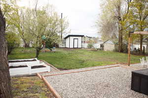 View of yard featuring a storage shed, a garden, a playground, fence, and an outdoor structure
