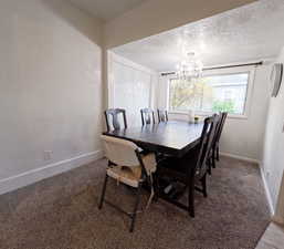 Carpeted dining area featuring a chandelier, a textured ceiling, and baseboards