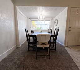 Carpeted dining space with a textured ceiling, baseboards, and an inviting chandelier