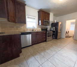 Kitchen featuring a sink, light stone countertops, washing machine and clothes dryer, tasteful backsplash, and appliances with stainless steel finishes