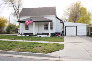 Bungalow-style home featuring concrete driveway, covered porch, an outbuilding, a front yard, and roof with shingles