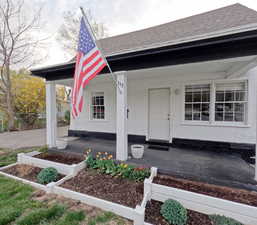 View of exterior entry with a porch, roof with shingles, and stucco siding