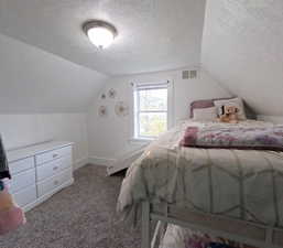 Bedroom with vaulted ceiling, visible vents, a textured ceiling, and carpet flooring