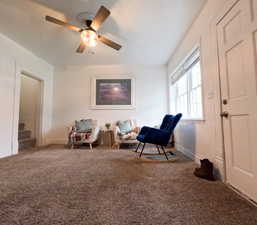 Living area featuring ceiling fan, baseboards, carpet flooring, and stairs