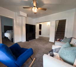 Carpeted living area with ceiling fan, baseboards, and stairs