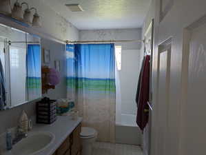 Full bath with a textured ceiling, vanity, shower / bath combination with curtain, toilet, and visible vents