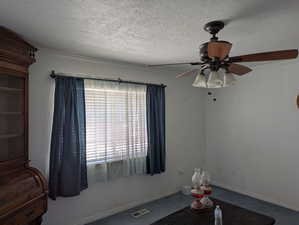 Interior space with a ceiling fan, a textured ceiling, and visible vents