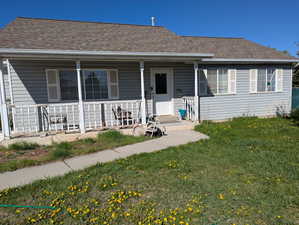Bungalow-style home with a front yard, a shingled roof, and covered porch