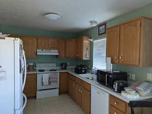 Kitchen featuring a sink, white appliances, light floors, light countertops, and under cabinet range hood