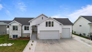 View of front of home featuring concrete driveway, central AC unit, stone siding, and a front yard