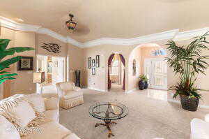 Living area with crown molding, arched walkways, carpet, and baseboards