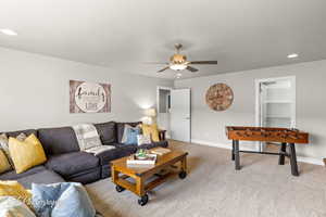 Carpeted living area with ceiling fan, baseboards, and recessed lighting