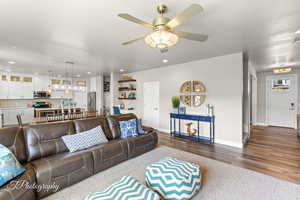 Living room with wood finished floors, ceiling fan with notable chandelier, and recessed lighting