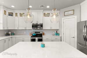 Kitchen with glass insert cabinets, stainless steel appliances, white cabinets, backsplash, and visible vents