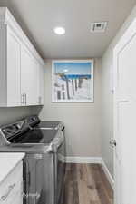 Clothes washing area with dark wood finished floors, visible vents, washing machine and dryer, baseboards, and cabinet space