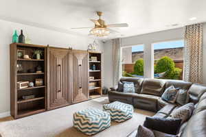 Carpeted living area with ceiling fan and visible vents