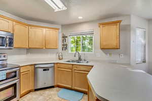 Kitchen featuring light countertops, light brown cabinets, stainless steel appliances, and a sink