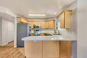 Kitchen with a peninsula, light brown cabinetry, a sink, light countertops, and appliances with stainless steel finishes