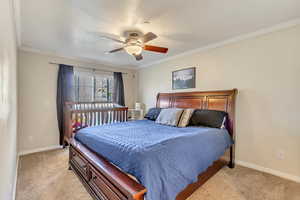 Bedroom featuring light carpet, a ceiling fan, baseboards, and ornamental molding