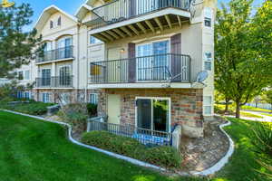 Rear view of property with stucco siding, a yard, stone siding, and a balcony