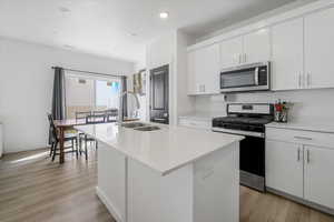 Kitchen featuring a sink, a center island with sink, recessed lighting, light countertops, and appliances with stainless steel finishes