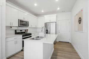 Kitchen featuring white cabinets, stainless steel appliances, light countertops, and a sink