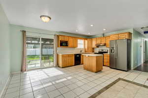 Kitchen featuring under cabinet range hood, light countertops, light tile patterned floors, a kitchen island, and black appliances