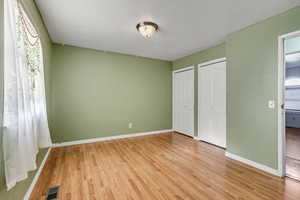 Unfurnished bedroom with two closets, baseboards, visible vents, and light wood-style flooring