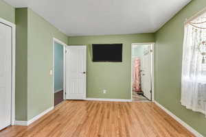 Unfurnished bedroom featuring light wood-type flooring, ensuite bath, and baseboards