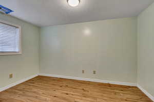 Spare room with light wood-type flooring, baseboards, and a textured ceiling