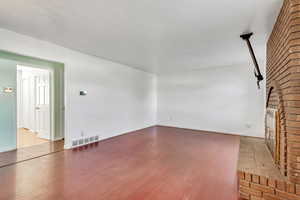 Unfurnished living room featuring baseboards, wood finished floors, visible vents, and a brick fireplace