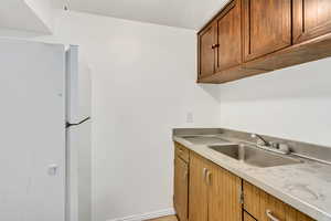 Kitchen with light countertops, freestanding refrigerator, a sink, and brown cabinets