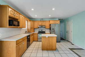 Kitchen featuring a center island, a sink, black appliances, light countertops, and under cabinet range hood