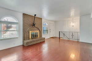 Unfurnished living room featuring wood-type flooring, a brick fireplace, baseboards, and an inviting chandelier