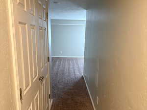 Hallway with carpet floors, baseboards, and a textured wall