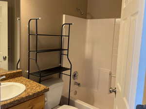 Bathroom with tile patterned floors, vanity, toilet, a textured wall, and washtub / shower combination