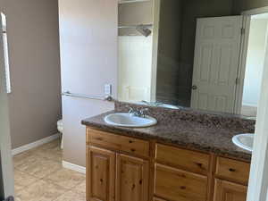 Bathroom with tile patterned flooring, double vanity, toilet, a sink, and baseboards