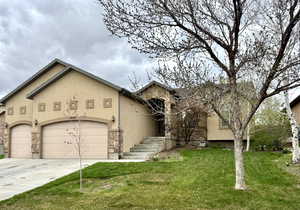 View of front facade with stone siding, concrete driveway, a garage, a front yard, and stucco siding