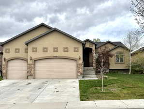View of front of property featuring concrete driveway, an attached garage, stucco siding, stone siding, and a front yard